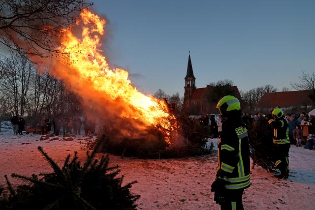 10 January 2026, Mecklenburg-Western Pomerania, Wustrow: Visitors enjoy warming themselves up at the traditional Christmas tree burning in the Bodden harbor of the Baltic Sea resort. Photo: Bernd Wüstneck/dpa