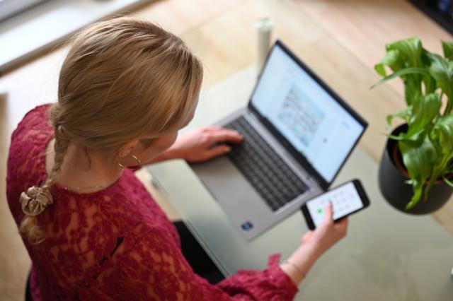 SYMBOL - 03 July 2024, Berlin: A woman sits at home at a glass table typing on a laptop, holding a smartphone in her right hand. According to a Verivox survey, the majority of German citizens have never used online administrative services such as ID card renewals or change of address notifications. Photo: Helena Dolderer/dpa
