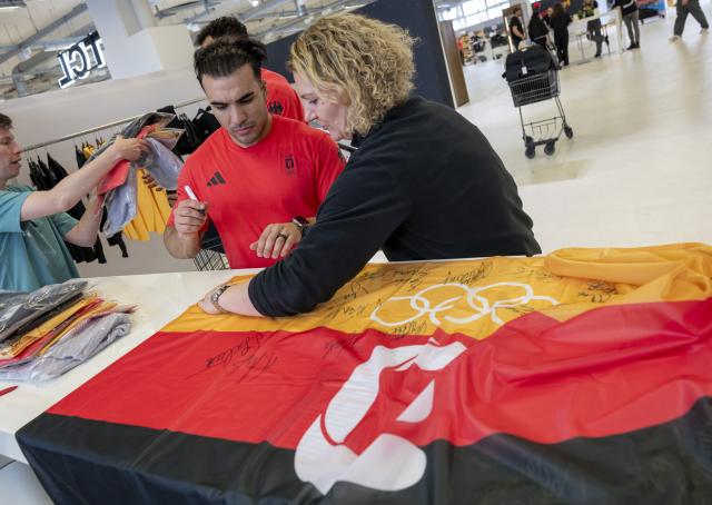 12 January 2026, Bavaria, Munich: German bobsledder Issam Ammour signs an autograph on a 'Team D' flag during the clothing fitting for the Olympic Winter Games Milano Cortina 2026. Photo: Peter Kneffel/dpa