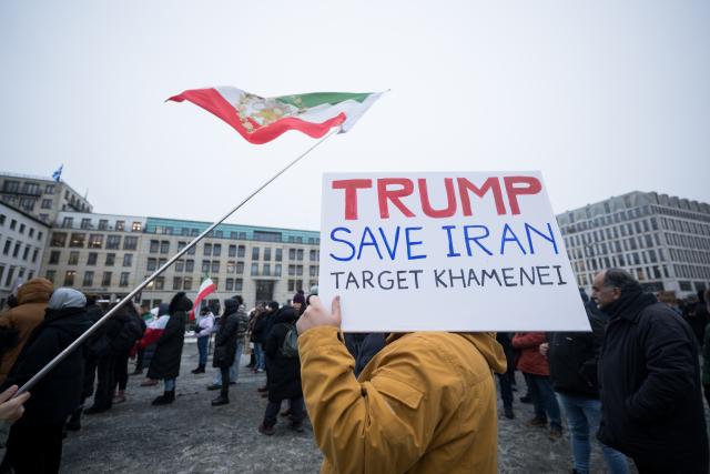 13 January 2026, Berlin: "Trump save Iran - Target Khamenei", reads a sign during a demonstration in support of the nationwide mass protests against the government in Iran on Paris Square. Above it hangs a flag with the image of Reza Pahlavi, son of the last Shah of Iran. Photo: Sebastian Christoph Gollnow/dpa