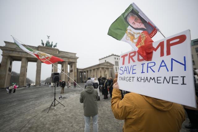 13 January 2026, Berlin: "Trump save Iran - Target Khamenei", reads a sign during a demonstration in support of the nationwide mass protests against the government in Iran on Paris Square. Above it hangs a flag with the image of Reza Pahlavi, son of the last Shah of Iran. Photo: Sebastian Christoph Gollnow/dpa