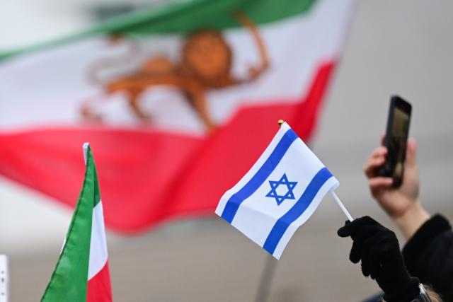 13 January 2026, Berlin: A woman holds an Israeli flag in front of an Iranian flag during a demonstration in support of the nationwide mass protests against the government in Iran on Paris Square. Photo: Sebastian Christoph Gollnow/dpa