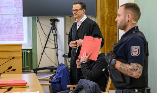 14 January 2026, Brandenburg, Cottbus: The defendant (C) shields his face with a file folder at the Cottbus Regional Court, as the murder trial begins. The case concerns the death of a Dresden police officer who was fatally struck by a car during an operation against fleeing car thieves in southern Brandenburg. Photo: Patrick Pleul/dpa