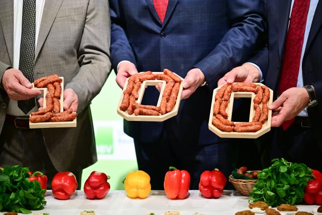 16 January 2026, Berlin: (L-R) Alois Rainer, Germany's Federal Minister for Food, Agriculture, and Rural Affairs, Joachim Rukwied, President of the German Farmers' Association, and Christophe Hansen, EU Commissioner for Agriculture and Food, hold a "100" made of sausages at the German Farmers' Association stand during the opening tour of the 90th International Green Week. Photo: Sebastian Christoph Gollnow/dpa