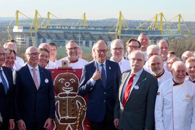 17 January 2026, North Rhine-Westphalia, Dortmund: Germany's Chancellor Friedrich Merz (C) stands between bakers in front of Signal Iduna Park after being awarded the 'Grosser Stutenkerl' by the West German Bakers' Guild. The roughly 1.2-metre-high, 10-kilogram baked figure has been awarded since 1988 to honor outstanding contributions to the baking trade. Photo: Bernd Thissen/dpa