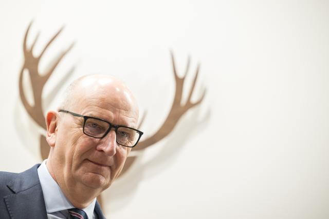 19 January 2026, Berlin: Dietmar Woidke, Minister President of Brandenburg, stands in front of a wooden figure of a stag during a tour of Brandenburg Day at the 90th International Green Week. The world's largest trade fair for food, agriculture and horticulture in Berlin is celebrating its 100th anniversary. Photo: Sebastian Christoph Gollnow/dpa