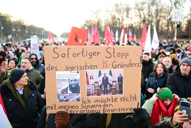 19 January 2026, Berlin: People hold a placardd says "Immediate halt to the Syrian IS founder. I do not want my taxes to finance terrorism" during a demonstration with the slogan "No welcome for Islamist Ahmed al-Sharaa in Berlin" against the visit of the Syrian interim president. The two-day visit planned for today has been postponed. Photo: Sebastian Christoph Gollnow/dpa