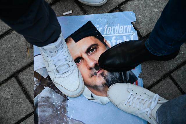 19 January 2026, Berlin: Participants stand over a picture of Ahmed al-Sharaa and former Syrian President Bashar al-Assad during a demonstration with the slogan "No welcome for Islamist Ahmed al-Sharaa in Berlin" against the visit of the Syrian transitional president. The two-day visit planned for today has been postponed. Photo: Sebastian Christoph Gollnow/dpa