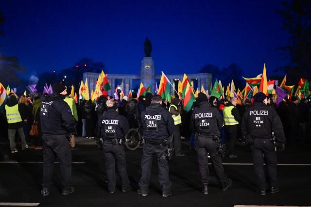 19 January 2026, Berlin: Police officers escort a large Kurdish flag during a demonstration with the slogan "No welcome for Islamist Ahmed al-Sharaa in Berlin" against the visit of the Syrian transitional president. The two-day visit planned for today has been postponed. Photo: Sebastian Christoph Gollnow/dpa