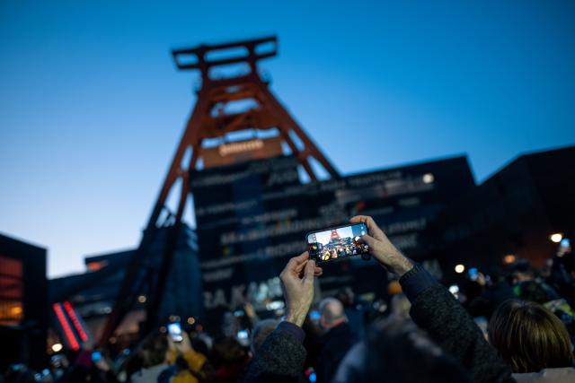 19 January 2026, North Rhine-Westphalia, Essen: A man holds a cell phone in the air and takes a photo at the Zollverein Coal Mine Industrial Complex in Essen, where a light installation by Bielefeld artist Hans-Christoph Muecke is projected onto the double trestle to mark the start of the campaign for an Olympic bid in North Rhine-Westphalia. Photo: Fabian Strauch/dpa