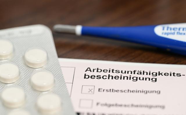 FILED - 18 November 2022, Baden-Württemberg, Stuttgart: A thermometer, medication, and a doctor's note certifying incapacity for work (sick note) lie on a bedside table. Photo: Bernd Weißbrod/dpa