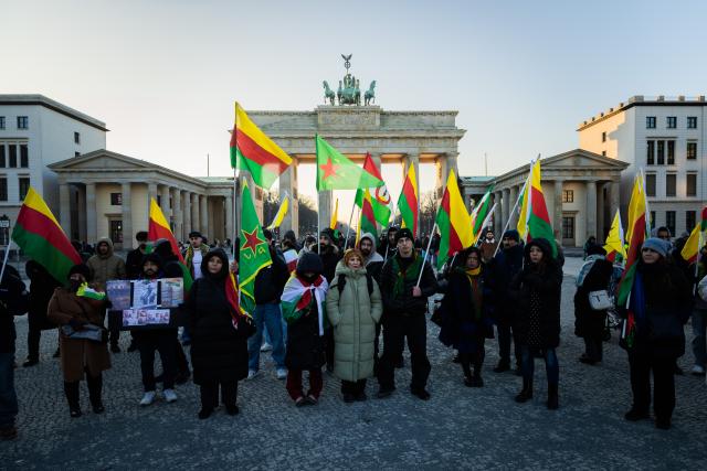 21 January 2026, Berlin: People stand with flags in front of the Brandenburg Gate during a rally in solidarity with Rojava, the Kurdish autonomous region in northeastern Syria. Photo: Christoph Soeder/dpa