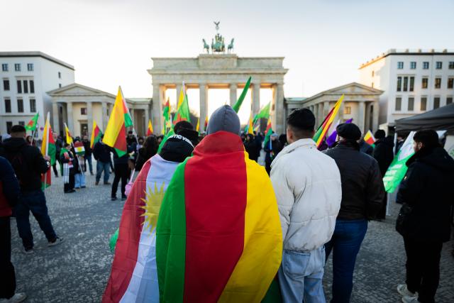 21 January 2026, Berlin: People stand with flags in front of the Brandenburg Gate during a rally in solidarity with Rojava, the Kurdish autonomous region in northeastern Syria. Photo: Christoph Soeder/dpa
