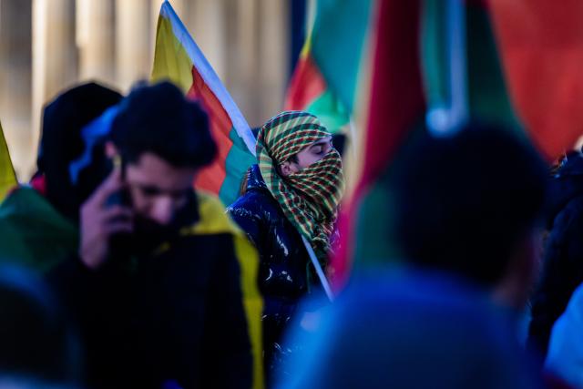 21 January 2026, Berlin: People stand with flags in front of the Brandenburg Gate during a rally in solidarity with Rojava, the Kurdish autonomous region in northeastern Syria. Photo: Christoph Soeder/dpa