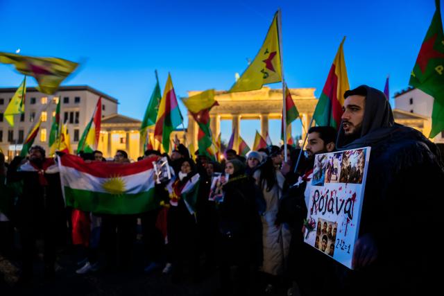 21 January 2026, Berlin: People stand with flags in front of the Brandenburg Gate during a rally in solidarity with Rojava, the Kurdish autonomous region in northeastern Syria. Photo: Christoph Soeder/dpa