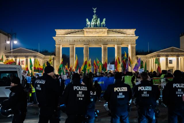 21 January 2026, Berlin: Police officers stand guard as people stand with flags in front of the Brandenburg Gate during a rally in solidarity with Rojava, the Kurdish autonomous region in northeastern Syria. Photo: Christoph Soeder/dpa
