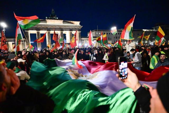 FILED - 19 January 2026, Berlin: Protesters carry a large Kurdish flag to the Brandenburg Gate during a demonstration with the slogan "No welcome for Islamist Ahmed al-Sharaa in Berlin" against the visit of the Syrian transitional president. The two-day visit planned for today has been postponed. Photo: Sebastian Christoph Gollnow/dpa