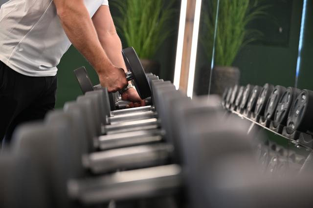 FILED - 01 April 2025, Cologne: A man stands at a weight bench in front of a mirror at the gym and lifts a dumbbell. Photo: Wolf von Dewitz/dpa