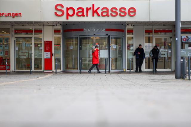 FILED - 12 January 2026, North Rhine-Westphalia, Gelsenkirchen: Security staff stand in front of the Sparkasse Gelsenkirchen branch, which remains closed after the spectacular break-in; a passer-by walks past. Photo: Christoph Reichwein/dpa
