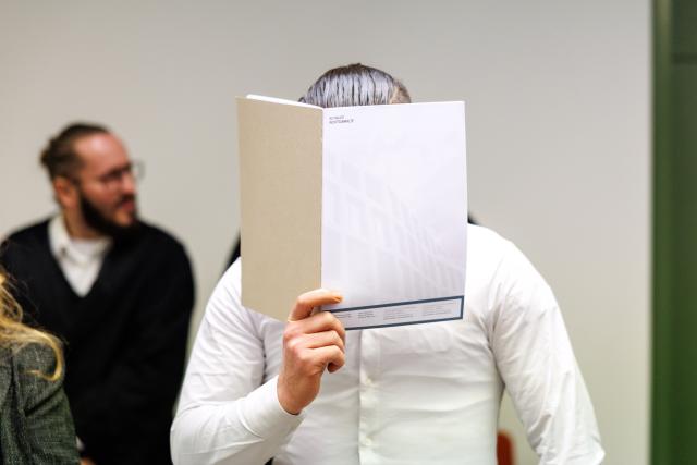 09 February 2026, Bavaria, Munich: A man accused by prosecutors of planning an attack in Germany using an explosive or incendiary device sits in a courtroom at a regional court ahead of the start of his trial, shielding his face with a folder, as his lawyer Norman Jacob sits in the background. Photo: Matthias Balk/dpa