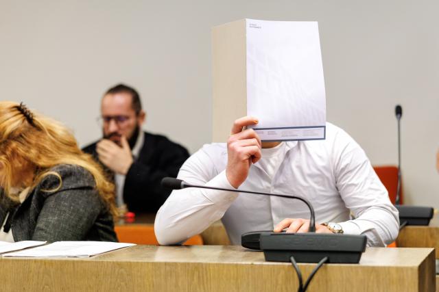 09 February 2026, Bavaria, Munich: A man accused by prosecutors of planning an attack in Germany using an explosive or incendiary device sits in a courtroom at a regional court ahead of the start of his trial, shielding his face with a folder, as his lawyer Norman Jacob sits in the background. Photo: Matthias Balk/dpa