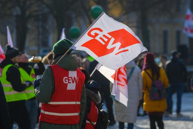 10 February 2026, Saxony-Anhalt, Magdeburg: A strike participant comes to Magdeburg Cathedral Square with a banner of the Education and Science Union (GEW). A GEW rally was held there. Numerous public sector employees in Saxony-Anhalt took part in warning strikes. The Education and Science Union (GEW) and the Verdi trade union had called for this. According to GEW, around 1,000 participants gathered in Magdeburg for a rally on the cathedral square. Photo: Klaus-Dietmar Gabbert/dpa