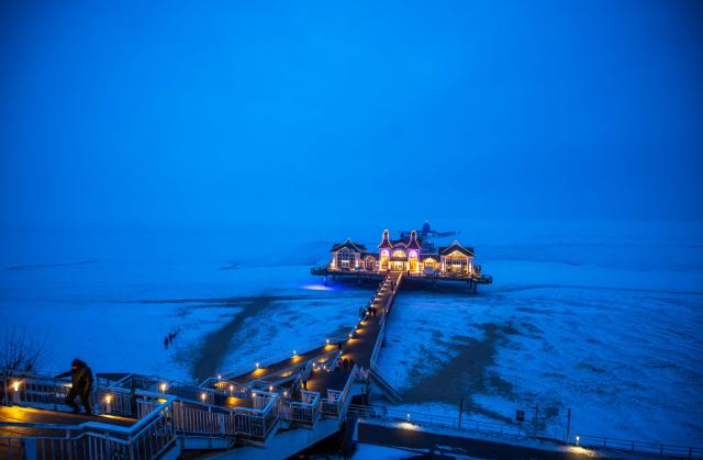 10 February 2026, Mecklenburg-Western Pomerania, Sellin: The pier on the Baltic Sea coast on the island of Ruegen surrounded by a closed ice cover is illuminated. Photo: Jens Büttner/dpa
