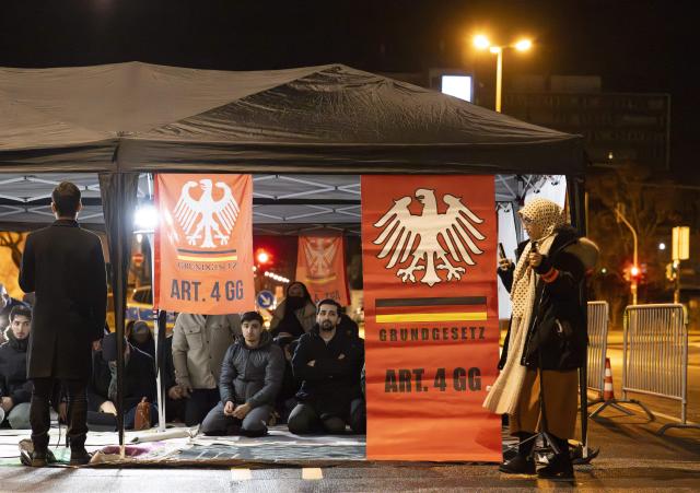12 February 2026, Hesse, Frankfurt/Main: Men and women pray under a pavilion set up on the street in front of the closed Imam Ali Mosque in Frankfurt. By displaying protest posters and referring to the fourth article of the Basic Law, the gathering under the slogan "Defend religious freedom: Hands off our mosque" is considered an approved protest action according to the administrative court. Photo: Boris Roessler/dpa