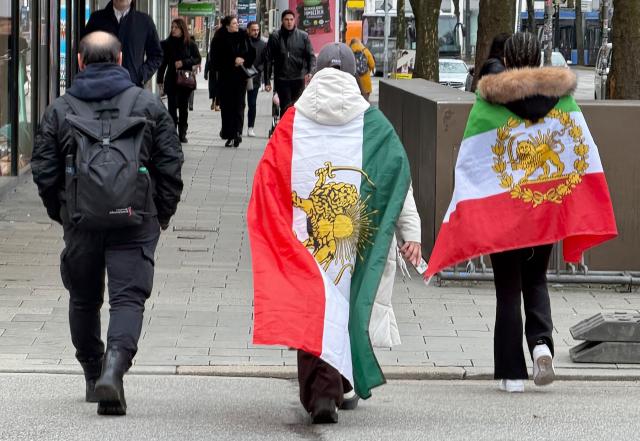 14 February 2026, Bavaria, Munich: People carrying various former flags of Iran walk through the city centre in Munich during a demonstration against the Iranian government on the sidelines of the Munich Security Conference, part of wider protests calling for change in Iran's political system. Photo: Marijan Murat/dpa