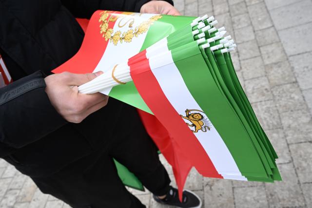 14 February 2026, Bavaria, Munich: Older Iranian flags featuring a lion and sun emblem are displayed at a demonstration on Theresienwiese under the slogan 'Human rights and freedom in Iran'. International solidarity with the Iranian people" on the sidelines of the Munich Security Conference, drawing attention to the human rights situation in Iran as part of wider protests calling for change in the country's political system. Photo: Felix Hörhager/dpa