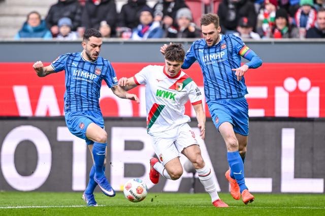 15 February 2026, Bavaria, Augsburg: Heidenheim's Arijon Ibrahimovic (L) and Patrick Mainka (R) battle for the ball with Augsburg's Mert Koemuer during the German Bundesliga soccer match between FC Augsburg and 1. FC Heidenheim at WWK Arena. Photo: Harry Langer/dpa - WICHTIGER HINWEIS: Gemäß den Vorgaben der DFL Deutsche Fußball Liga bzw. des DFB Deutscher Fußball-Bund ist es untersagt, in dem Stadion und/oder vom Spiel angefertigte Fotoaufnahmen in Form von Sequenzbildern und/oder videoähnlichen Fotostrecken zu verwerten bzw. verwerten zu lassen.