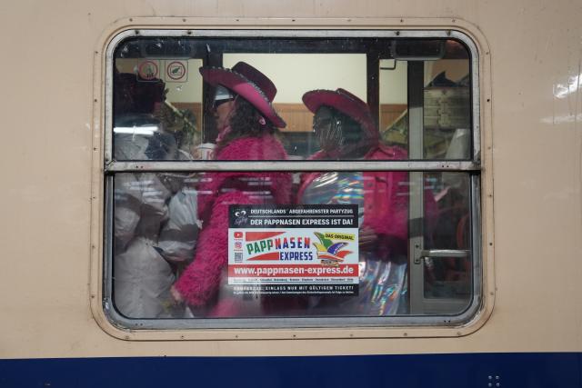 16 February 2026, Bremen: Dressed-up carnivalists walk through a compartment of the Pappnasen Express train on the journey from Hamburg to Cologne as it departs from Bremen station. Hundreds of carnival revellers once again travel on the Pappnasenexpress to Rose Monday in Cologne. Photo: Marcus Brandt/dpa