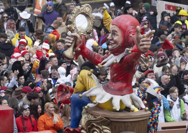 16 February 2026, Rhineland-Palatinate, Mainz: A float with a larger-than-life jester figure makes its way through the city during the Rose Monday parade. Mainz Cathedral can be seen in the background, while firefighters accompany the procession on a vehicle. Thousands of spectators follow the procession through the city center. The "foolish lindworm" includes political floats, "Schwellkoeppe", marching bands, flag bearers and guards. The length of the parade route is over seven kilometers. Photo: Boris Roessler/dpa