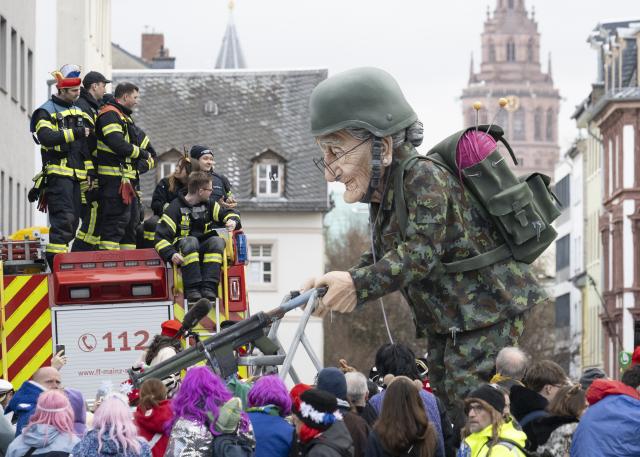 16 February 2026, Rhineland-Palatinate, Mainz: A float shows an armed figure in uniform. Thousands of spectators follow the parade through the city center. The "foolish lindworm" includes political floats, "Schwellkoeppe", marching bands, flag bearers and guards. The parade route is over seven kilometers long. Photo: Boris Roessler/dpa