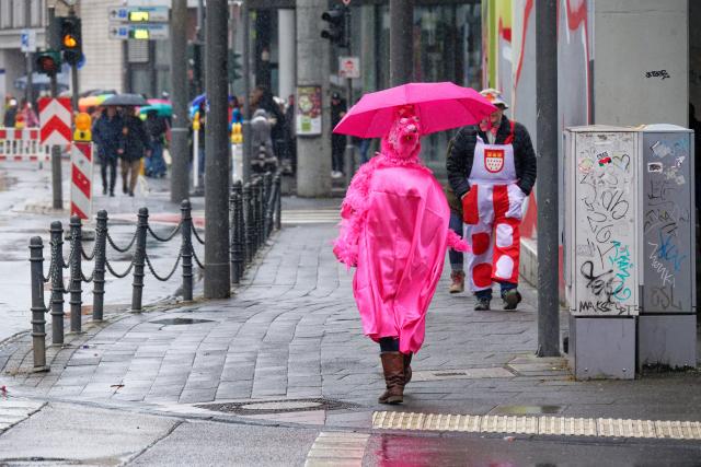 16 February 2026, North Rhine-Westphalia, Cologne: A carnival woman protects herself from the rain at the edge of the Rose Monday parade. Photo: Henning Kaiser/dpa