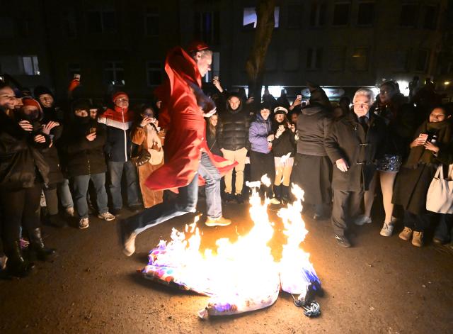 18 February 2026, North Rhine-Westphalia, Cologne: Carnival revellers jump over the burning Nubbel doll in front of the Ubier-Schaenke in Cologne. The Nubbel is a straw doll that serves as a scapegoat for "transgressions" committed during the carnival, such as excessive drinking or partying. Photo: Roberto Pfeil/dpa