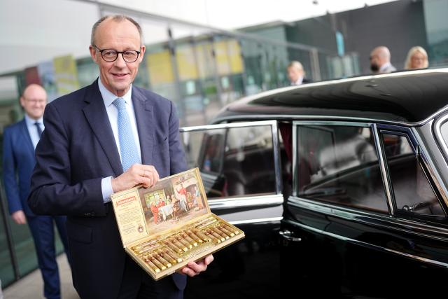 19 February 2026, Baden-Württemberg, Stuttgart: German Chancellor Friedrich Merz shows a cigar box from former Chancellor Adenauer's Mercedes in front of the exhibition hall during a tour of the hall before the CDU federal party conference. New presidium and board members will be elected on Friday. For the third time in a row, Merz is the only candidate for the chairmanship. Photo: Kay Nietfeld/dpa