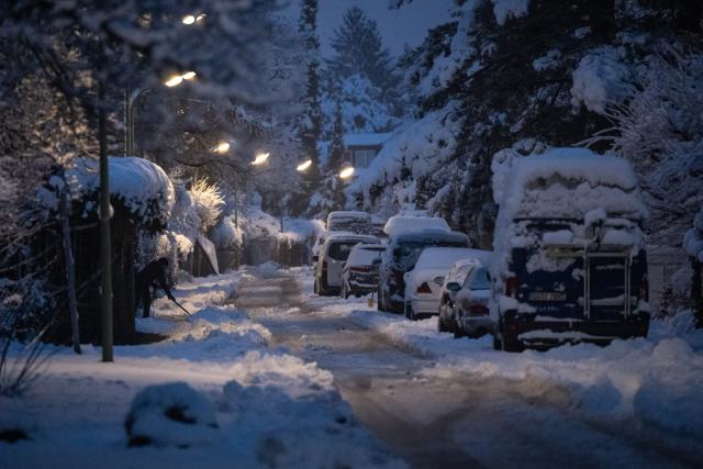 20 February 2026, Bavaria, Munich: A person shovels snow from a sidewalk in a narrow street with parked cars. Photo: Lukas Barth-Tuttas/dpa
