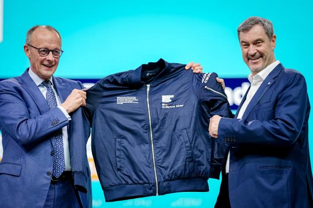21 February 2026, Baden-Württemberg, Stuttgart: German Chancellor Friedrich Merz (L) presents Markus Soeder, CSU Chairman and Minister President of Bavaria, with a jacket bearing the inscription European Space Agency on stage at the CDU federal party conference. After the board elections, the second day of the party conference will focus on content. Among other things, motions on part-time work, restricting social media use for children and pension reform will be discussed. Photo: Kay Nietfeld/dpa