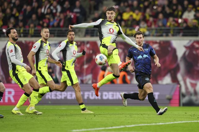 21 February 2026, Saxony, Leipzig: Borussia Dortmund's Luca Reggiani (C) saves a ball from Leipzig's Willi Orban (R) during the German Bundesliga soccer match between RB Leipzig and Borussia Dortmund at Red Bull Arena. Photo: Jan Woitas/dpa - WICHTIGER HINWEIS: Gemäß den Vorgaben der DFL Deutsche Fußball Liga bzw. des DFB Deutscher Fußball-Bund ist es untersagt, in dem Stadion und/oder vom Spiel angefertigte Fotoaufnahmen in Form von Sequenzbildern und/oder videoähnlichen Fotostrecken zu verwerten bzw. verwerten zu lassen.