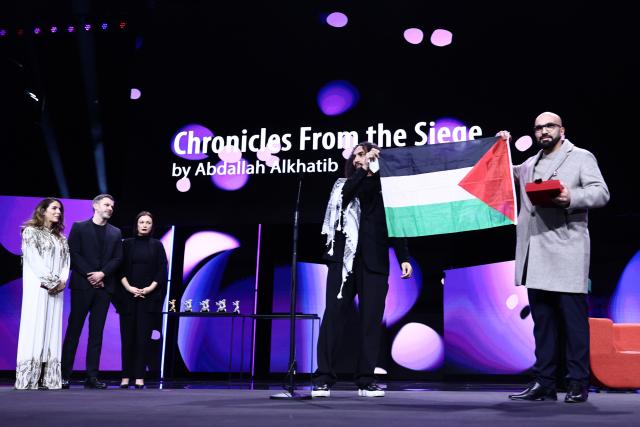 21 February 2026, Berlin: Palestinian director Abdallah Alkhatib (2nd R) receives the GWFF Award for Best Feature Film Debut for "Chronicles from the Siege" and holds up a Palestinian flag on stage during the award ceremony at the closing gala of the 76th Berlin International Film Festival. Photo: Christoph Soeder/dpa