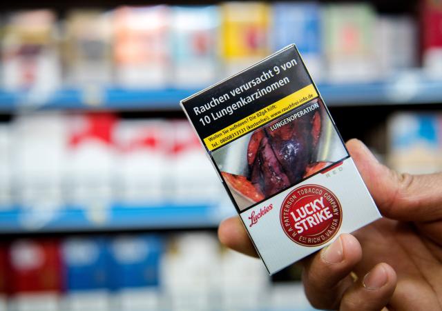 FILED - 26 June 2016, Hamburg: A man holds up a pack of 'Lucky Strike' cigarettes with a graphic warning in a kiosk in Hamburg. Photo: picture alliance / dpa