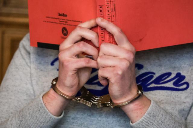 23 February 2026, Bremen: One of the defendants covers his face at Bremen Regional Court. A 19-year-old and a 35-year-old have been charged with conspiring to carry out a jihadist-motivated attack on a hospital in Bremerhaven in the summer of 2025. Photo: Focke Strangmann/dpa