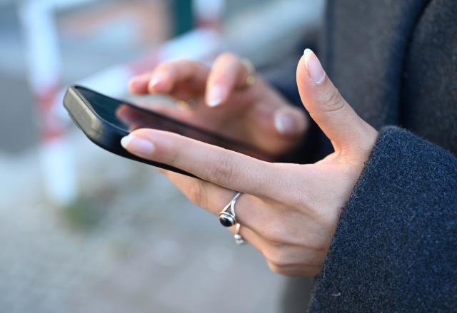 FILED - 19 January 2026, Berlin: A young woman stands on the sidewalk with her smartphone. (staged scene) Photo: Elisa Schu/dpa