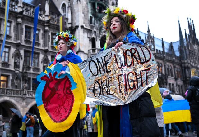 24 February 2026, Bavaria, Munich: Two women take part in a rally on Marienplatz on the fourth anniversary of Russia's attack on Ukraine, holding a poster with the slogan "One World - One Fight." Photo: Sven Hoppe/dpa