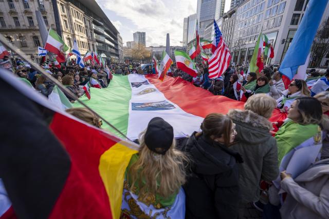 28 February 2026, Hesse, Frankfurt_Main: Rally participants hold an oversized national flag of Iran as well as the national flags of Germany and the United States, among others. On social media, the Homgarayi Frankfurt group had called for a "peaceful demonstration and march for freedom and democracy in Iran." Photo: Andreas Arnold/dpa
