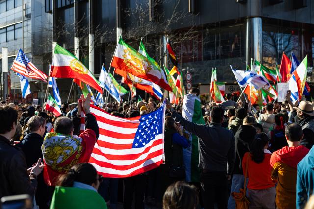 01 March 2026, Lower Saxony, Hanover: Demonstrators hold flags during a rally with the slogan "Human rights in Iran - solidarity with the civilian population" at Ernst-August-Platz in front of the main train station in Hanover. Photo: Michael Matthey/dpa
