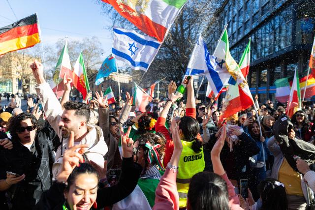 01 March 2026, Lower Saxony, Hanover: Demonstrators hold flags during a rally with the slogan "Human rights in Iran - solidarity with the civilian population" at Ernst-August-Platz in front of the main train station in Hanover. Photo: Michael Matthey/dpa