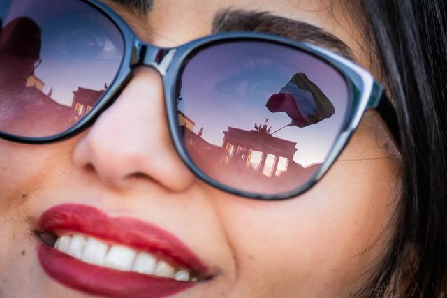 01 March 2026, Berlin: A flag is reflected in sunglasses of a woman during a demonstration against the Iranian mullah regime on Pariser Platz in front of the Brandenburg Gate. Photo: Christoph Soeder/dpa