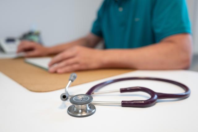 FILED - 27 May 2025, Saxony, Dresden: A family doctor sits at a desk next to a stethoscope in a consulting room of his GP practice and works on a computer. Photo: Sebastian Kahnert/dpa